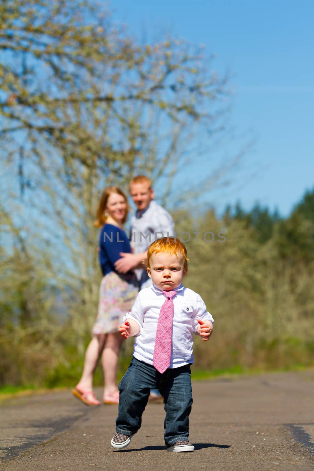 Parents are out of focus in this selective focus image while a baby boy runs toward the camera.