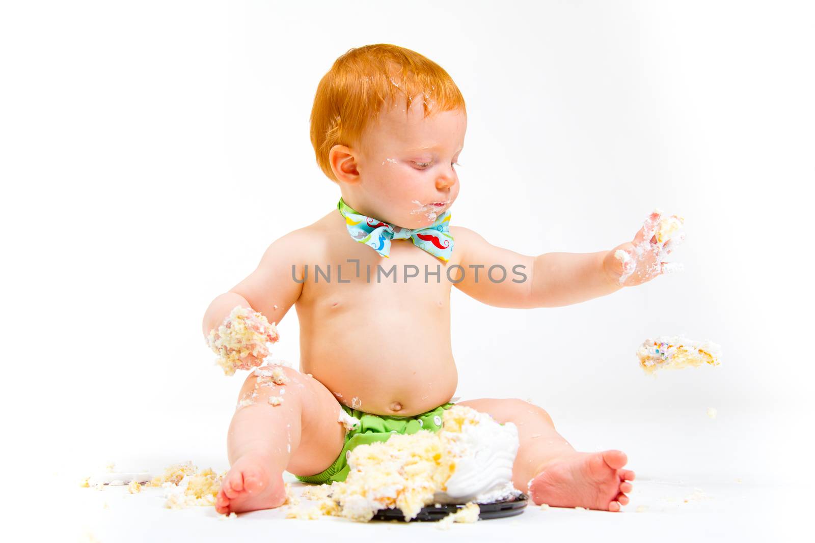 A baby boy gets to eat cake for the first time on his first birthday in this cake smash in studio against a white background.