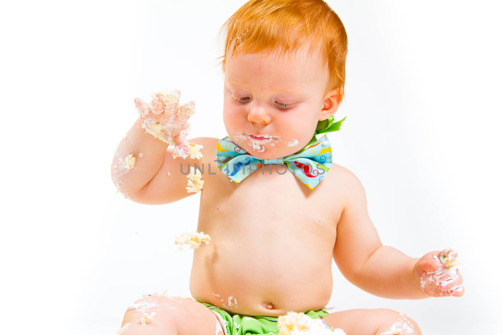 A baby boy gets to eat cake for the first time on his first birthday in this cake smash in studio against a white background.