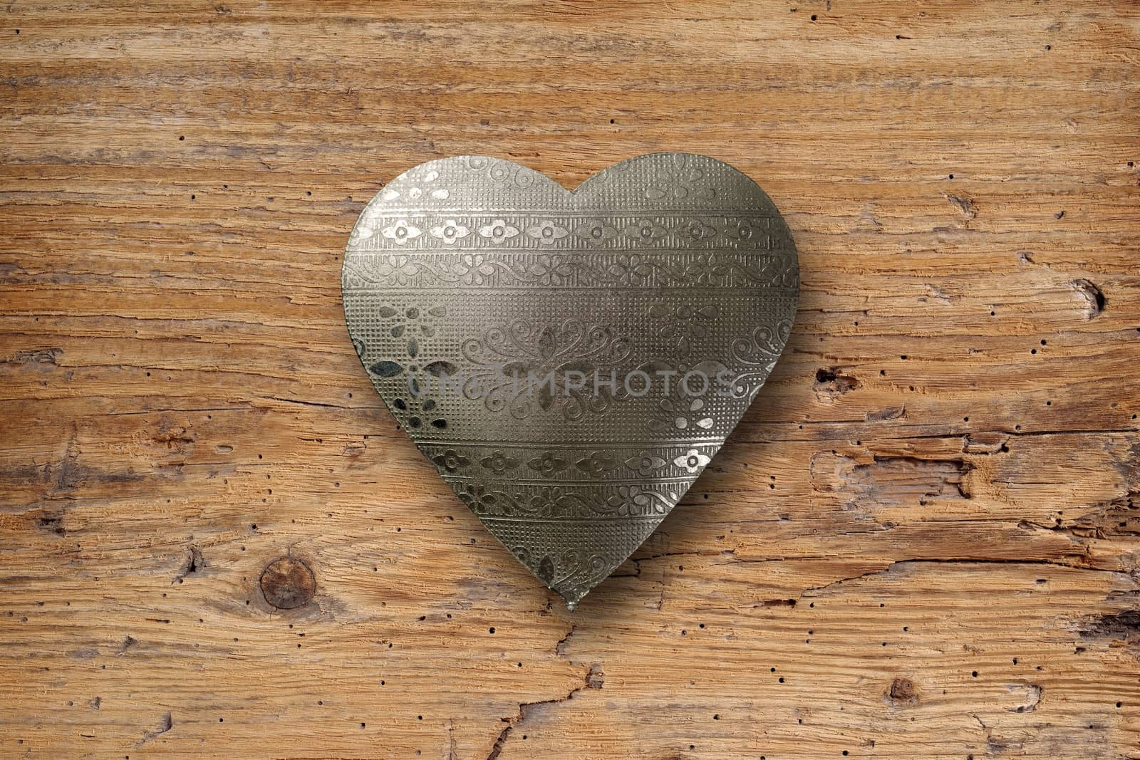 Photo of an ornate metal heart on top of an old plank of wood.
