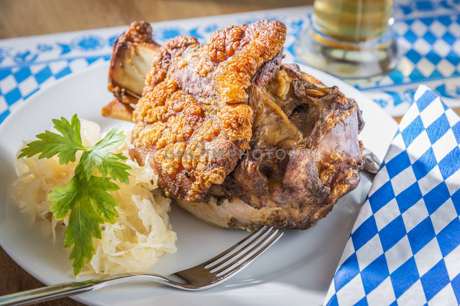 Oktoberfest pork hock with cabbage on a table with beer and Bavarian white blue napkin and fork