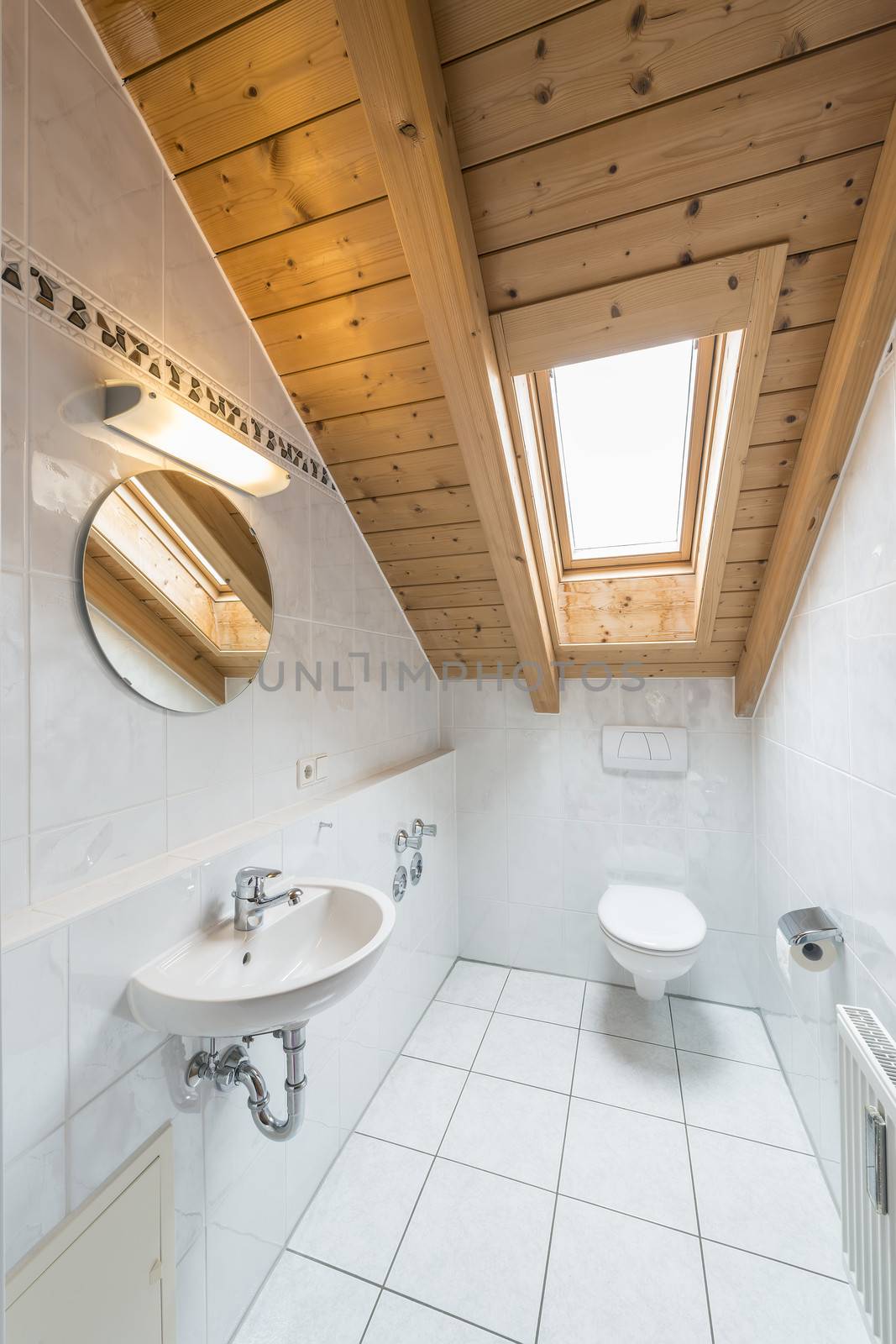 picture of a white tiled restroom with tiolet, basin, mirror and light.