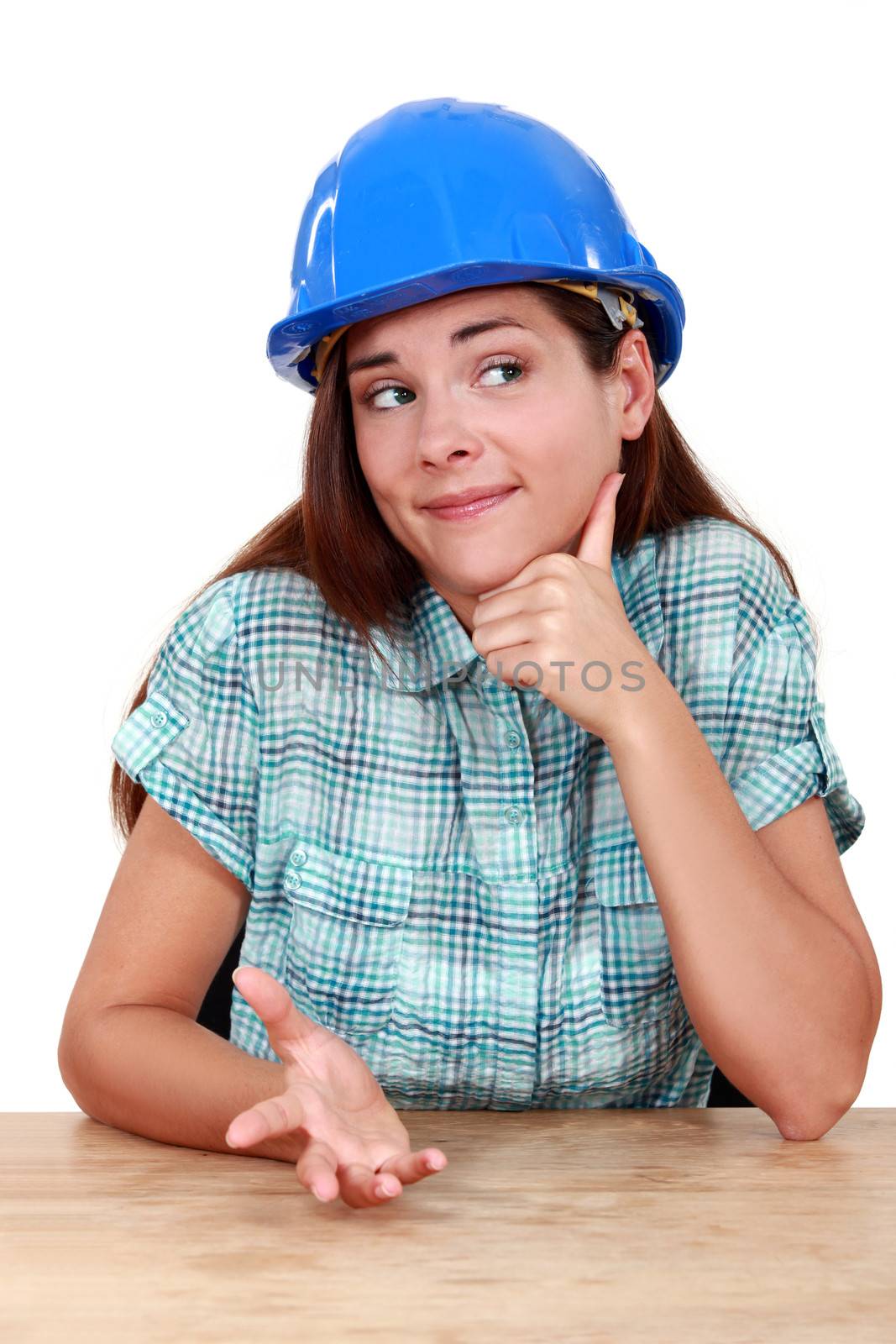 Thoughtful woman in a hardhat sitting at a desk by phovoir