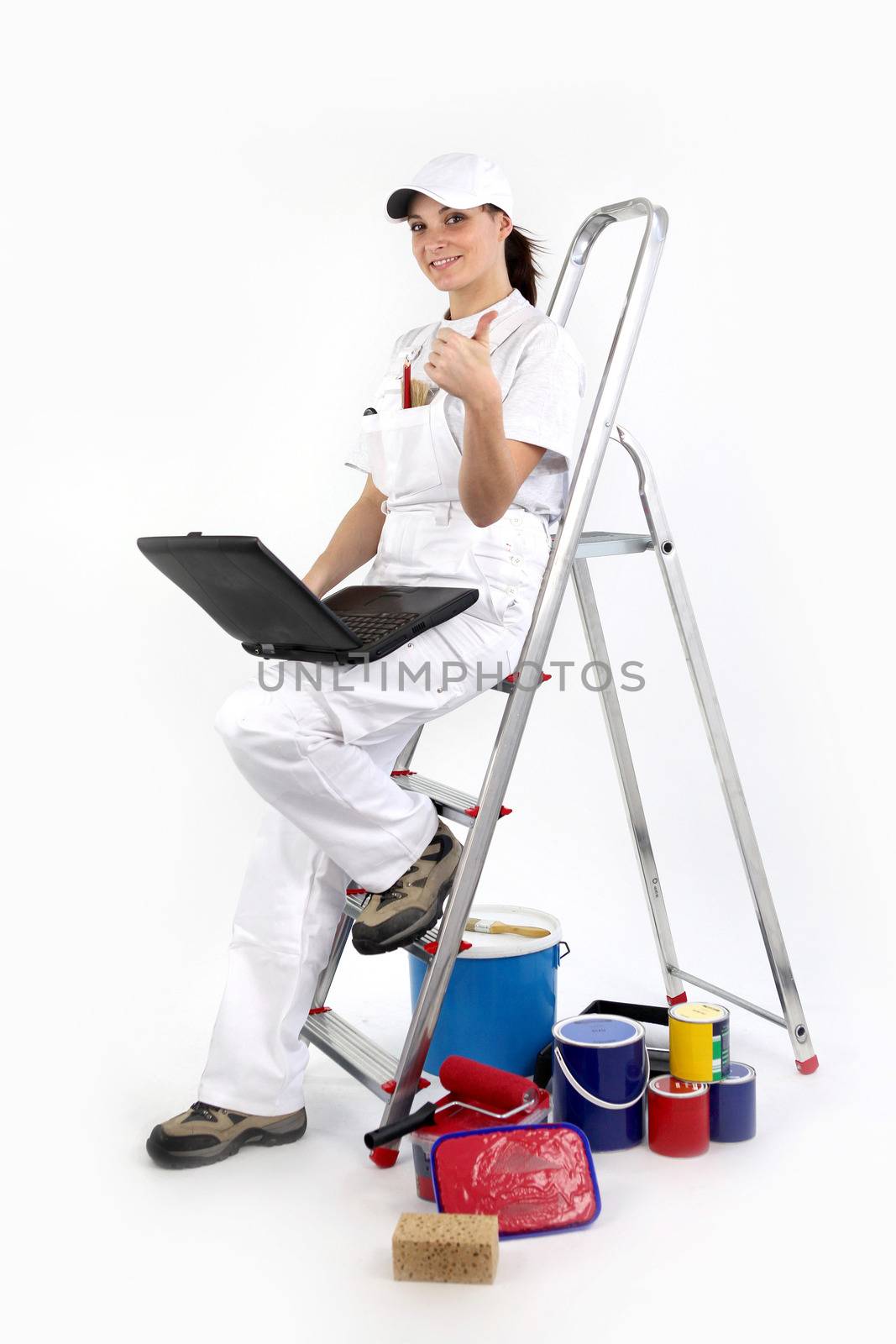 portrait of female painter decorator with laptop leaning against ladder