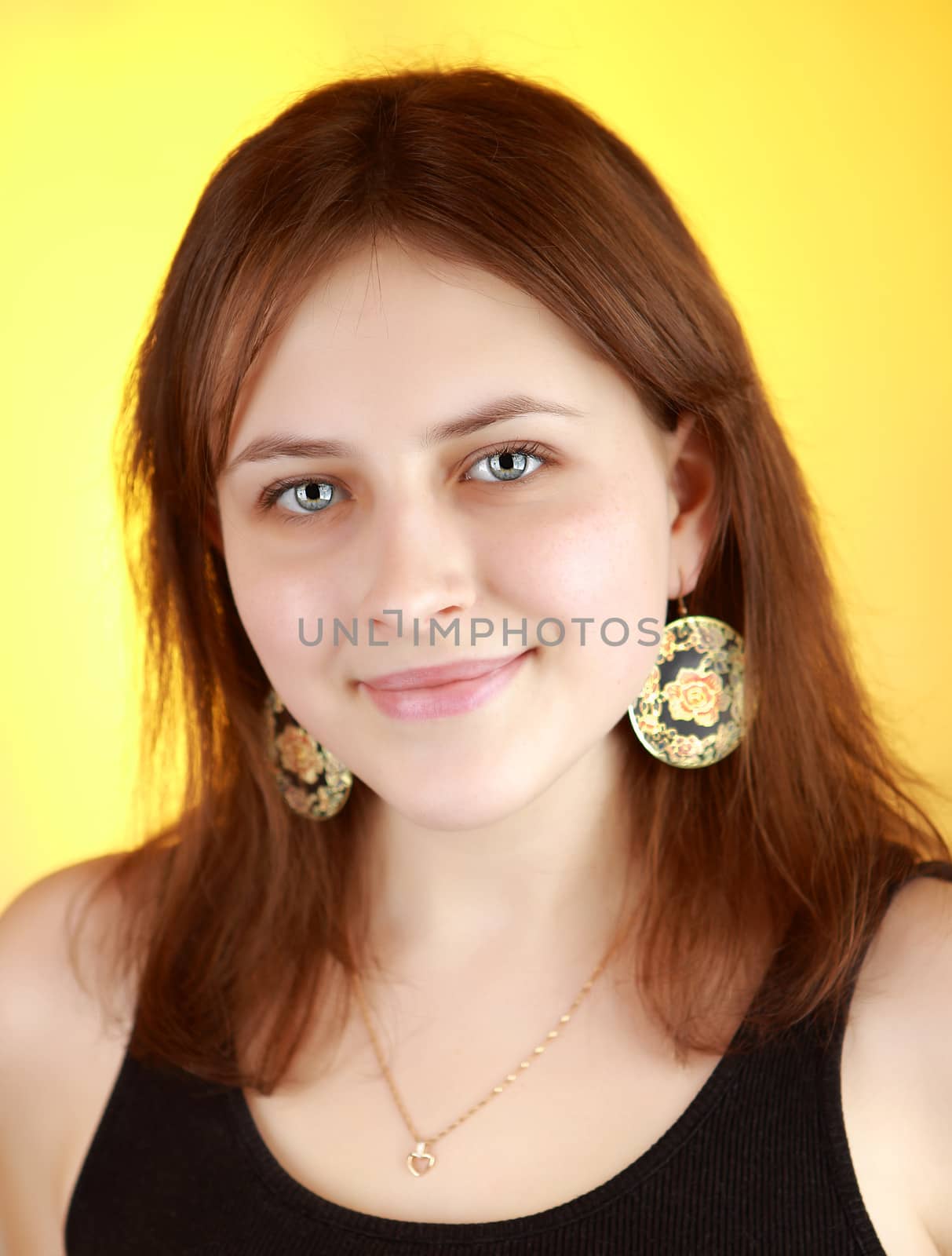 Teen girl 17 years old, light brown shoulder-length hair, wearing a black T-shirt, in the ears of big earrings, Vertical portrait on yellow background.