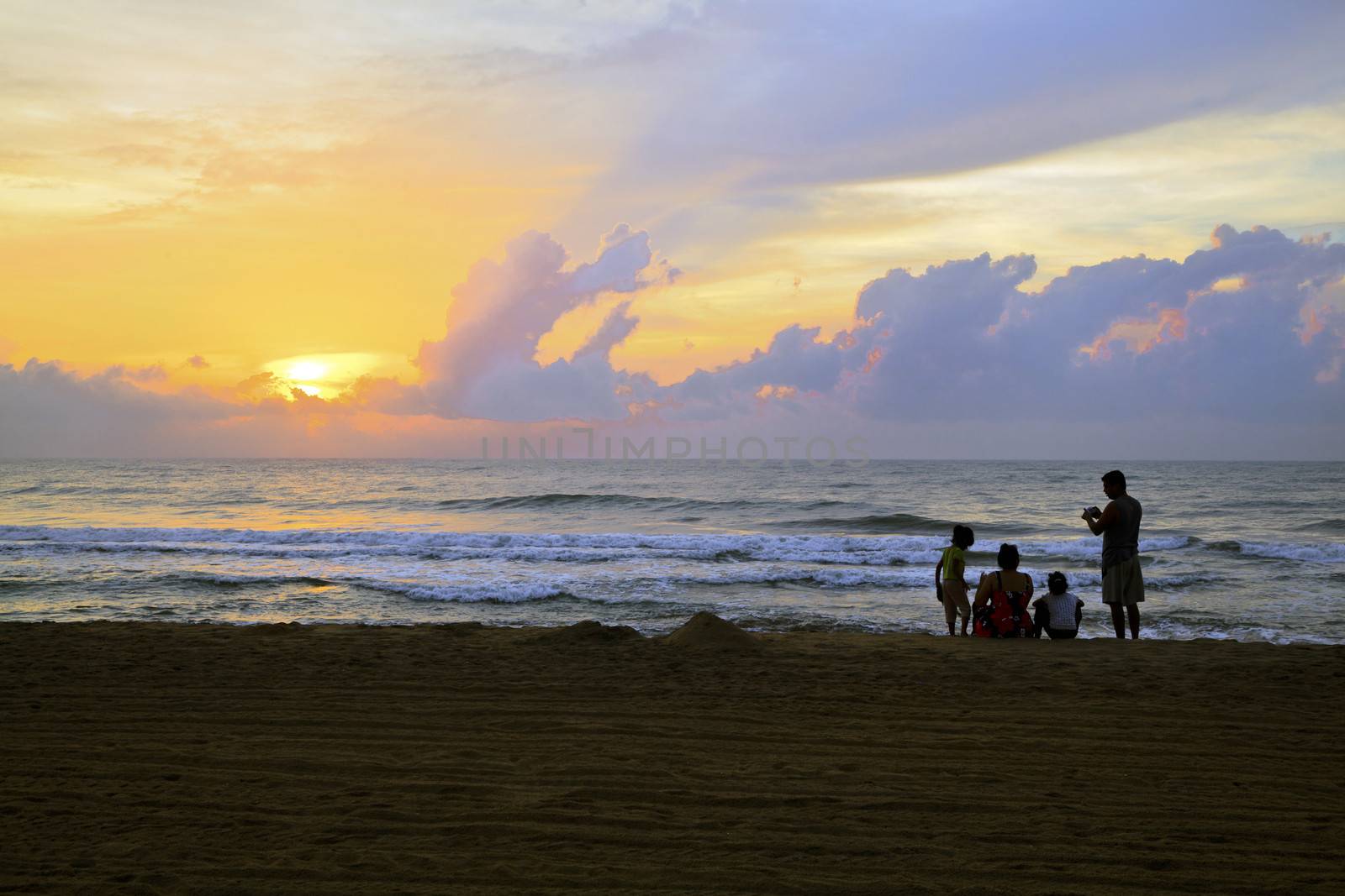 Horizontal color landscape of an Asian Indian family down on the beach early to catch the sunrise and family photographs. Man, woman and two kids captured at Manaputti Beach, Pondicherry, India