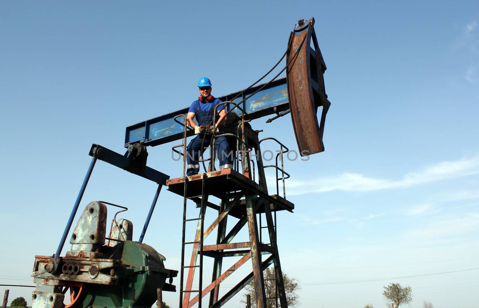 strong oil worker standing on pump jack by goce