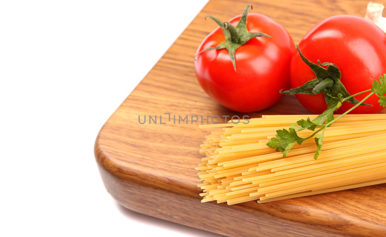 uncooked spaghetti, garlic and tomatos on a preparation board are located left