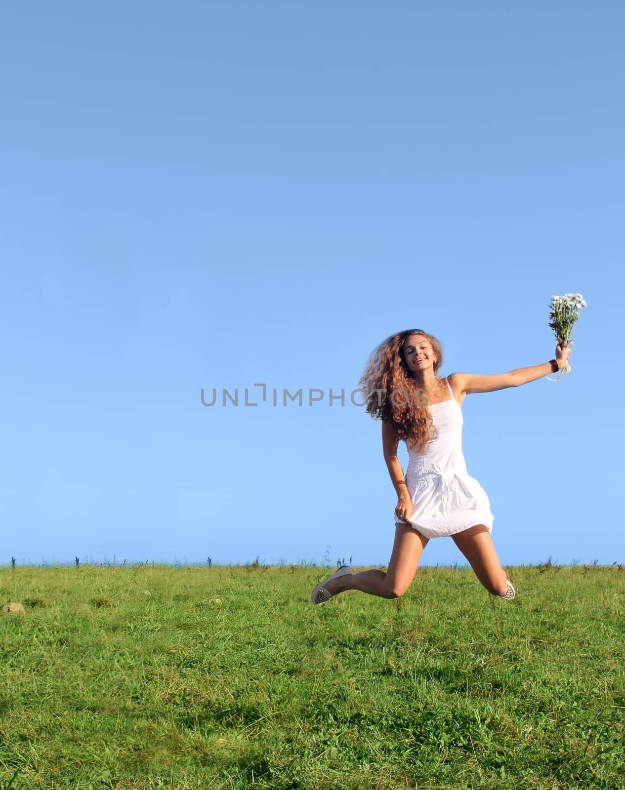 Beautiful girl in white dress jumping on green field