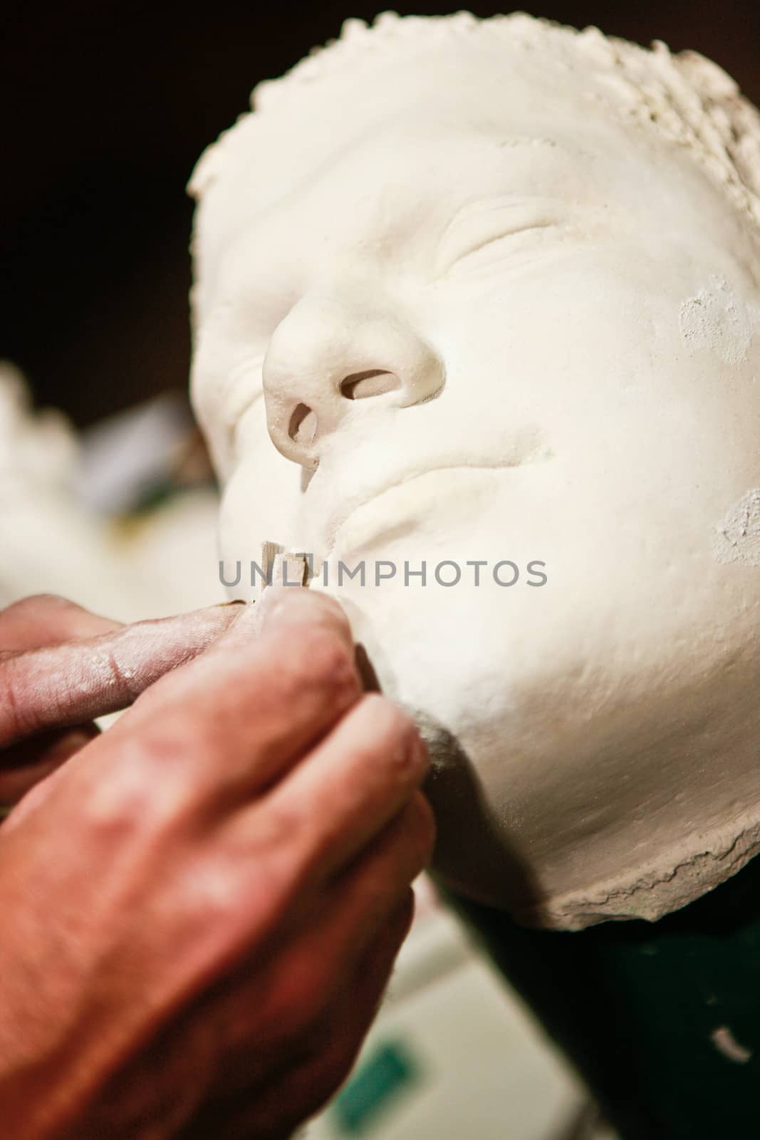 Artist working on a clay sculpture of a mans face adding texture and detail to the lips