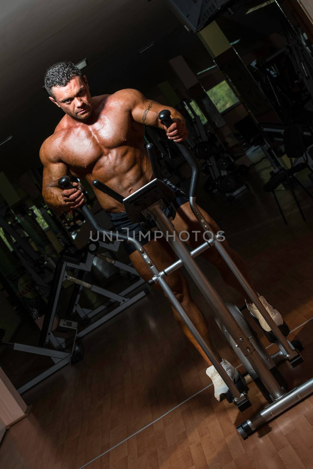 male bodybuilder using the elliptical machine by JalePhoto