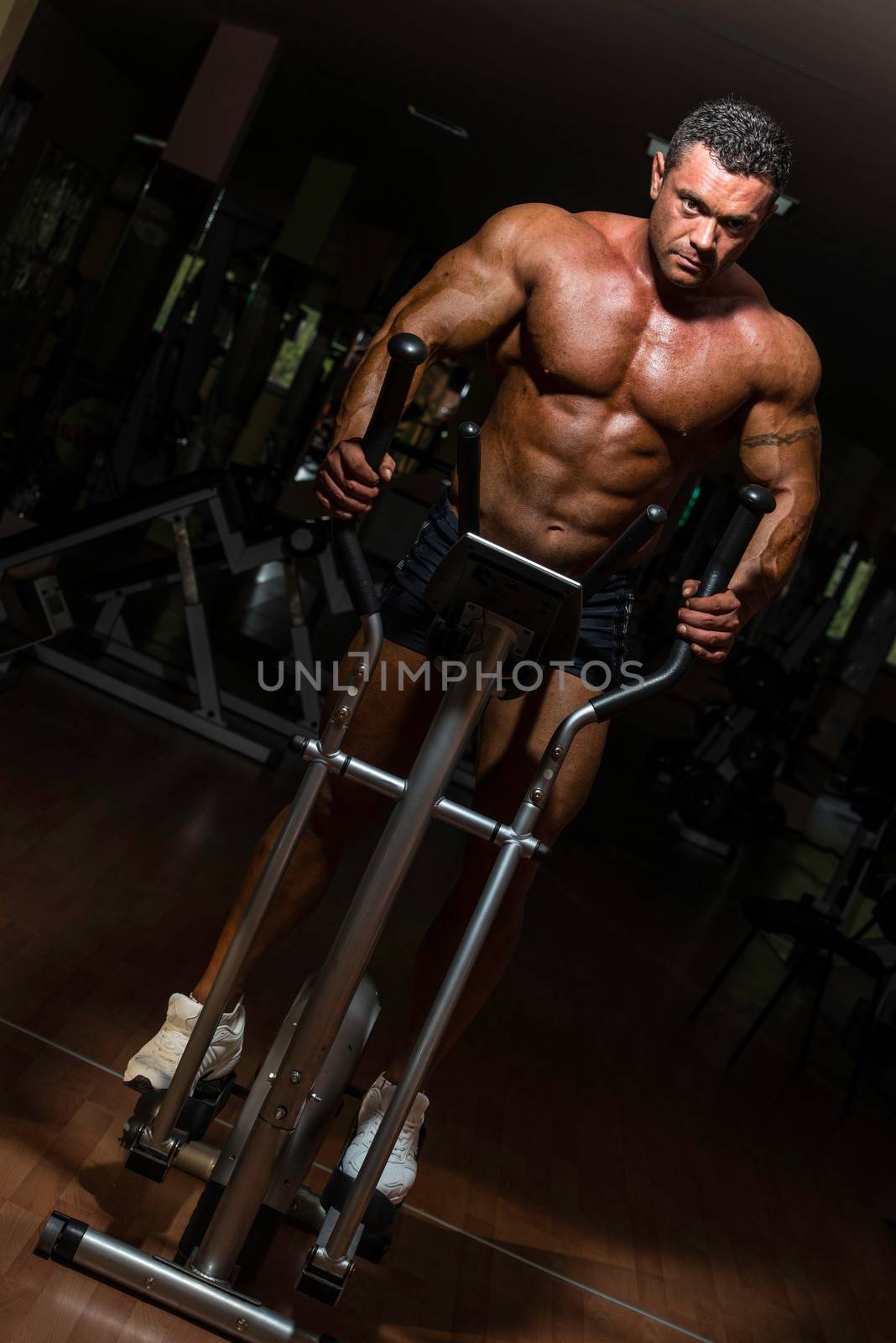male bodybuilder using the elliptical machine by JalePhoto