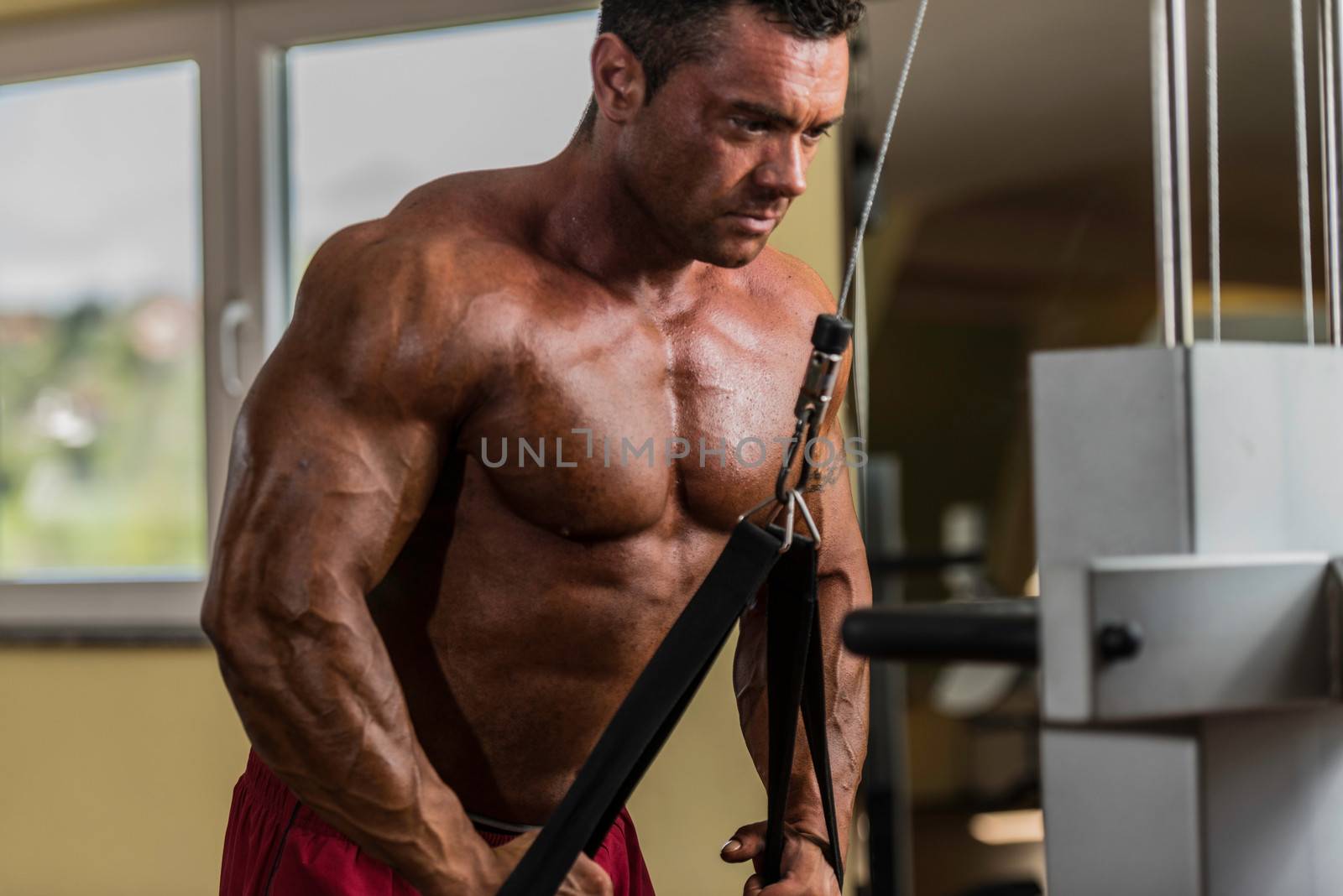 bodybuilder doing heavy weight exercise for triceps with cable