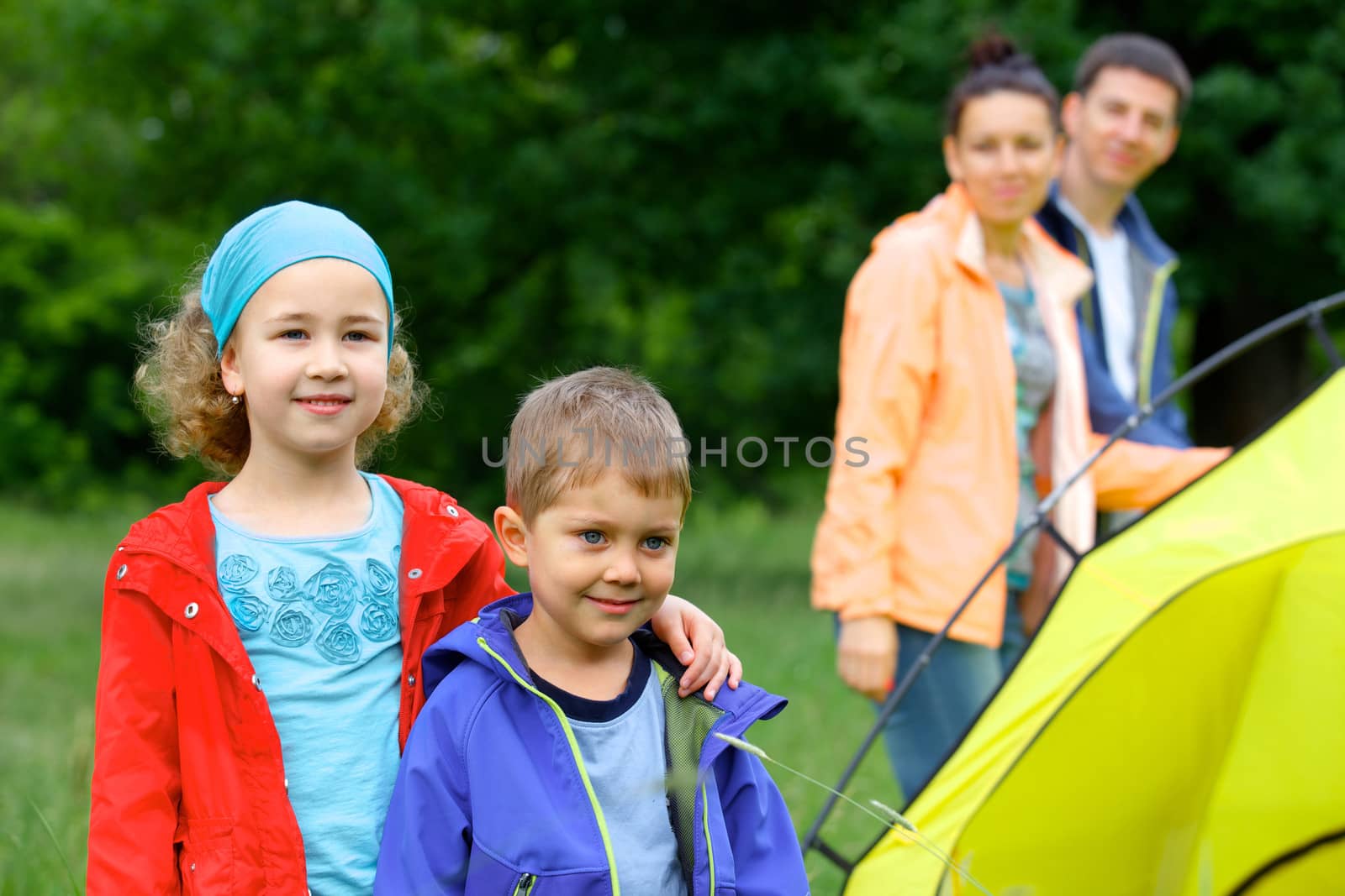 Summer, family camping - lovely sister and brother with parents near camp tent