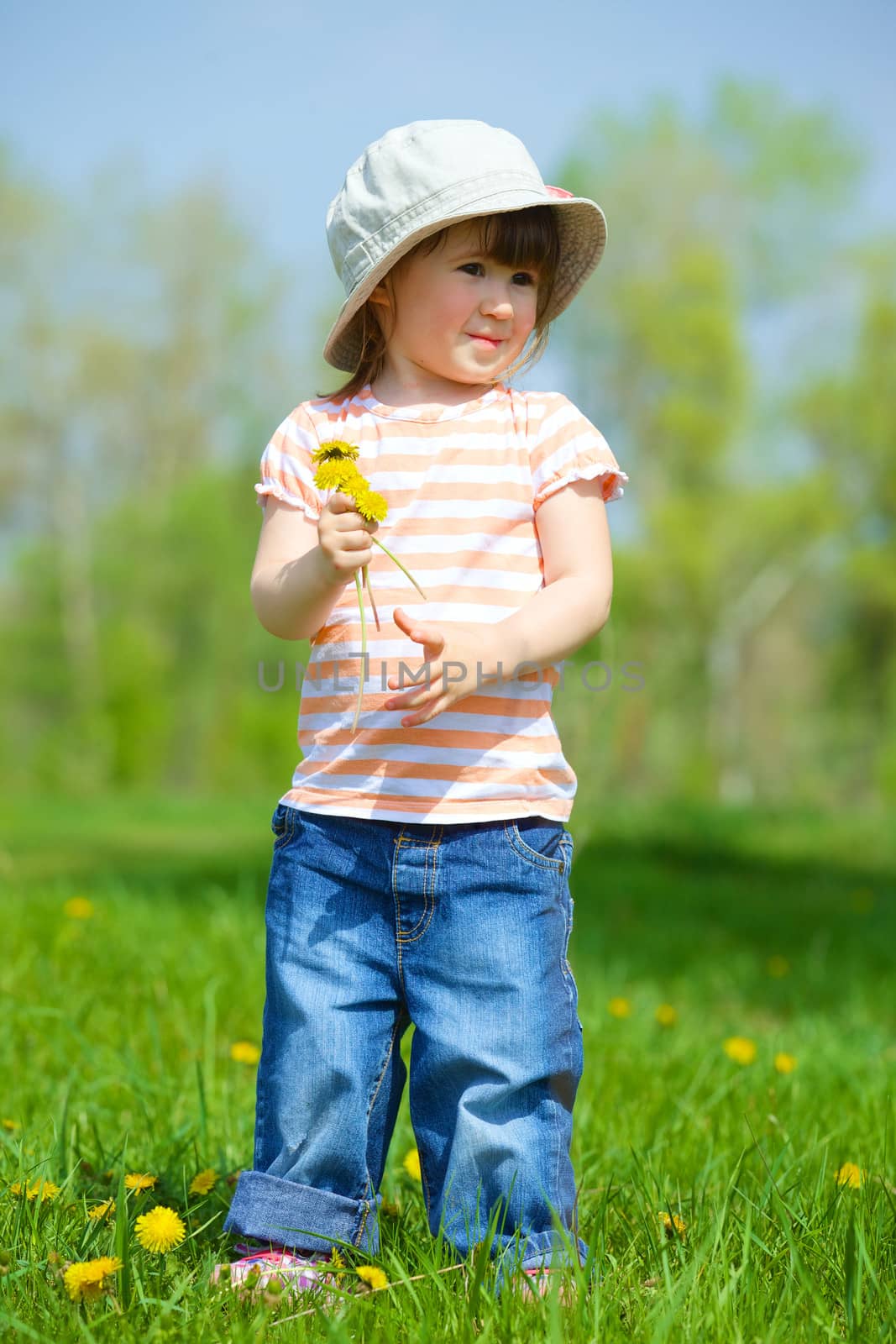 Sweet beautiful girl sitting on a green meadow with dandelions