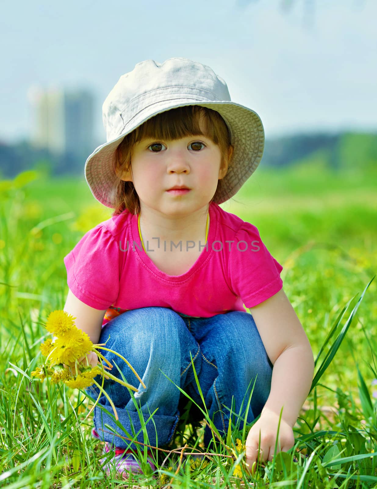 Sweet beautiful girl sitting on a green meadow with dandelions
