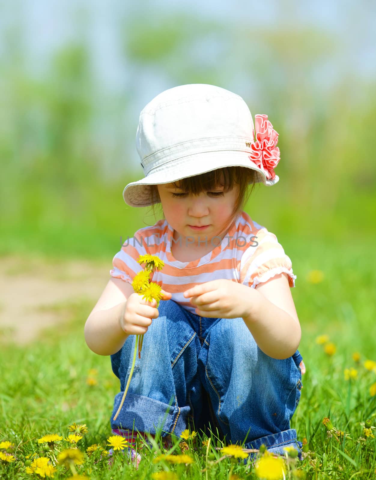 Sweet beautiful girl sitting on a green meadow with dandelions