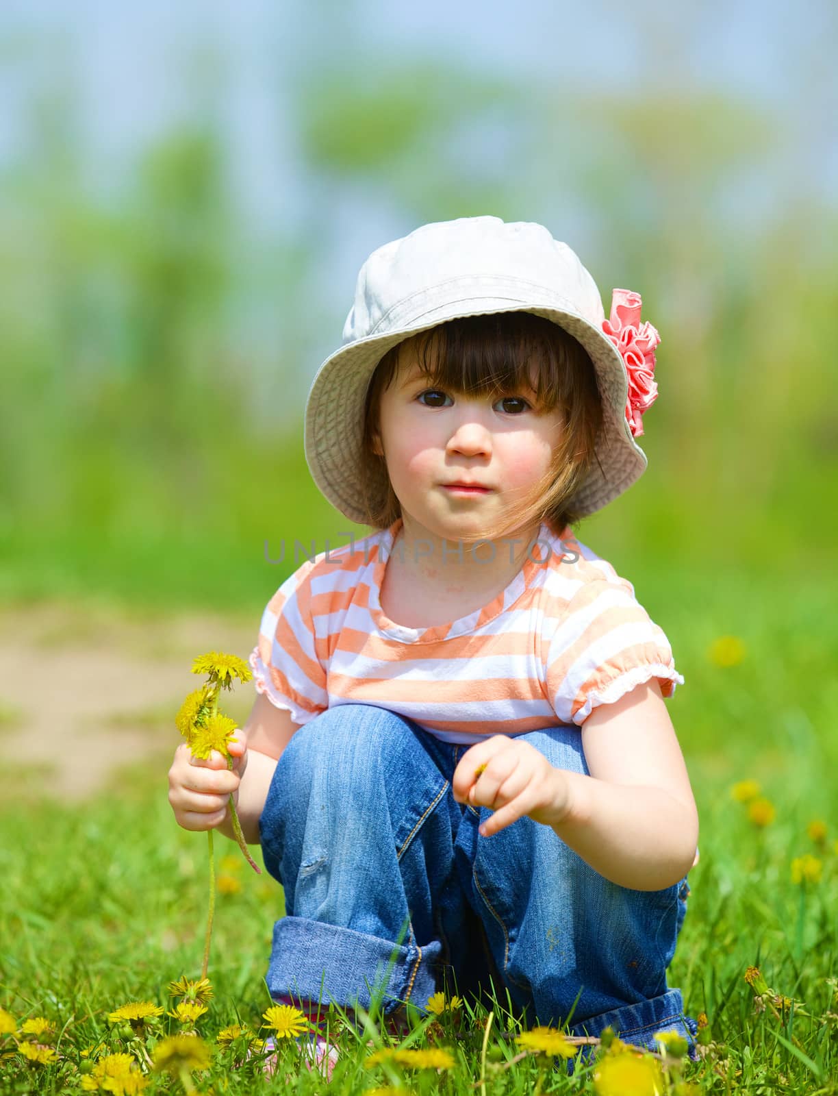 Sweet beautiful girl sitting on a green meadow with dandelions