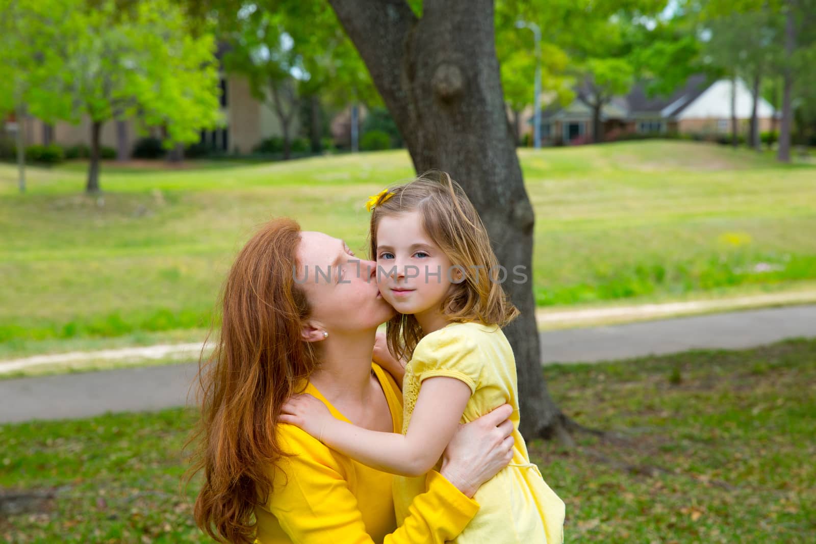 Mother kissing her blond daughter in green park by lunamarina