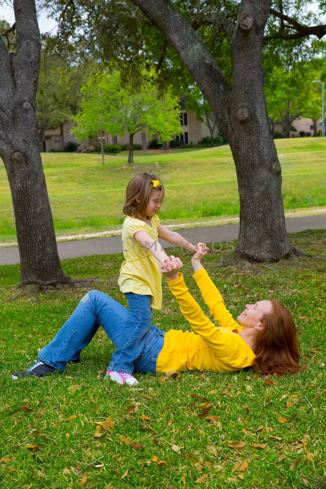 Daughter and mother playing lying on park lawn outdoor dressed in yellow