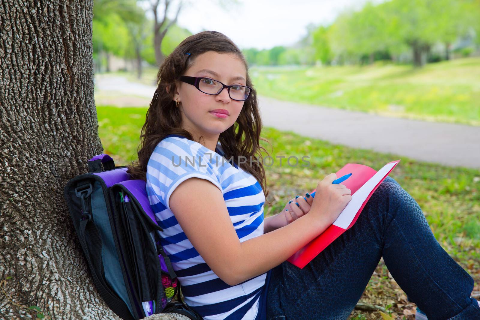 Clever student teenager girl with school bag resting relaxed under park tree