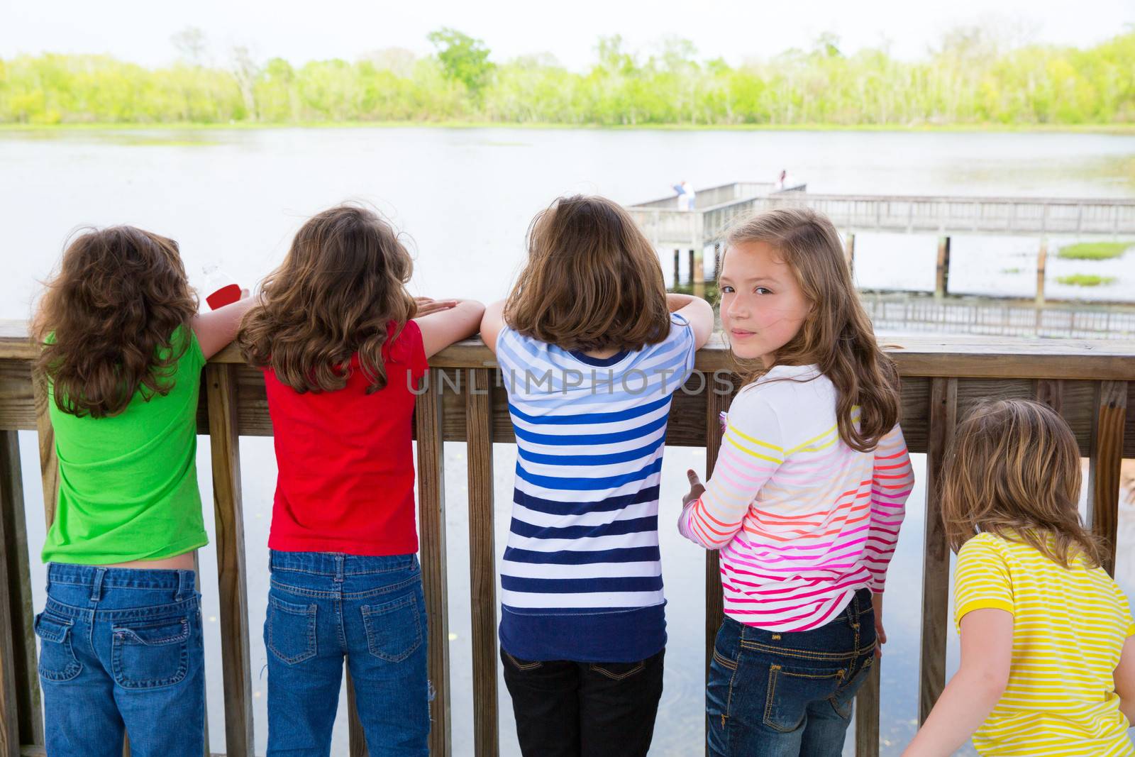 Children girls rear view looking at lake on railing and one looking behind