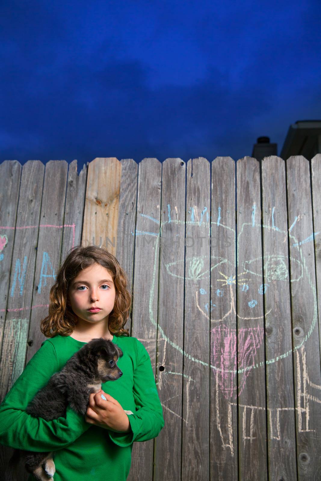 children girl holding puppy dog after chalk painting on backyard wood fence