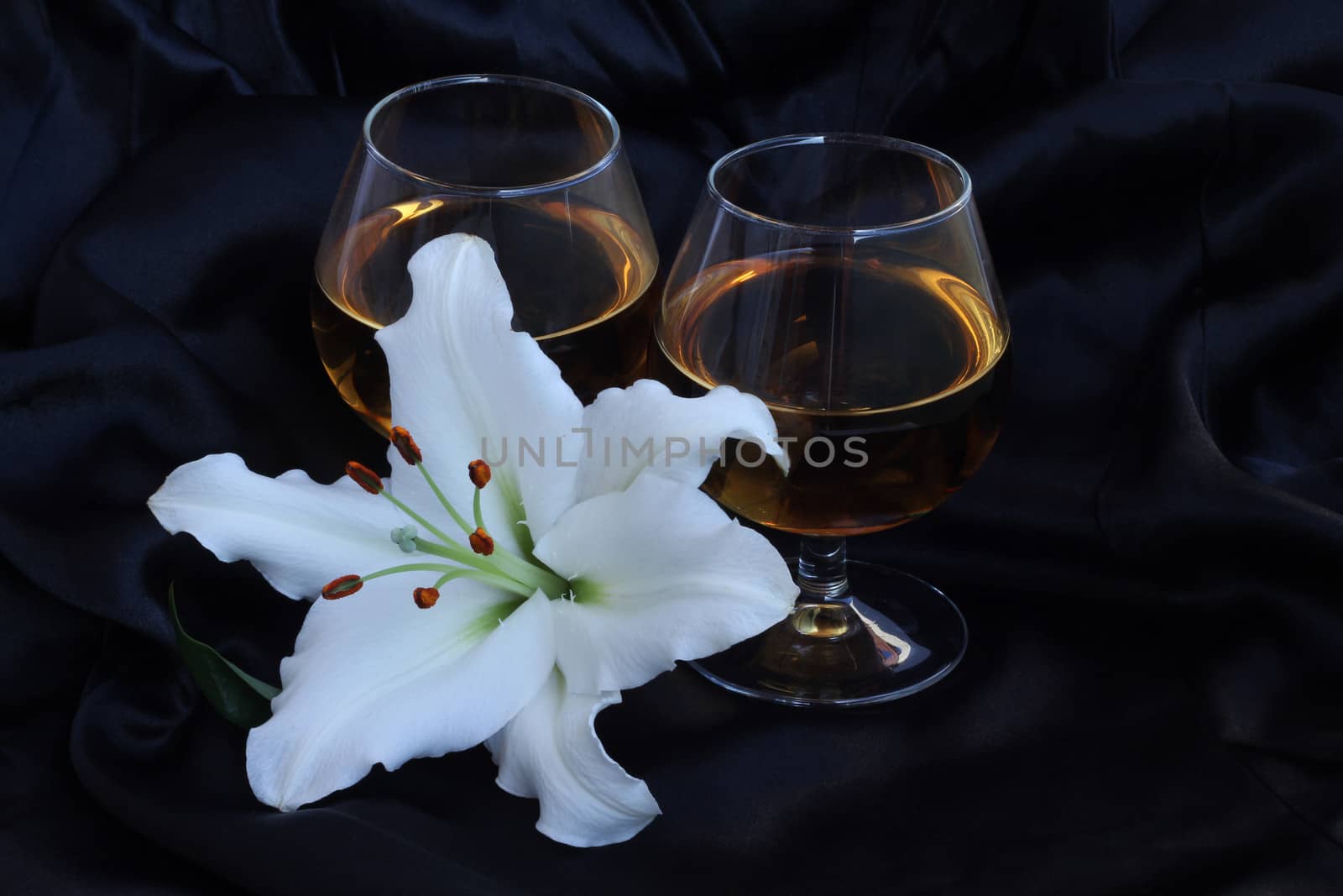 Glasses with wine and lily flower on black silk