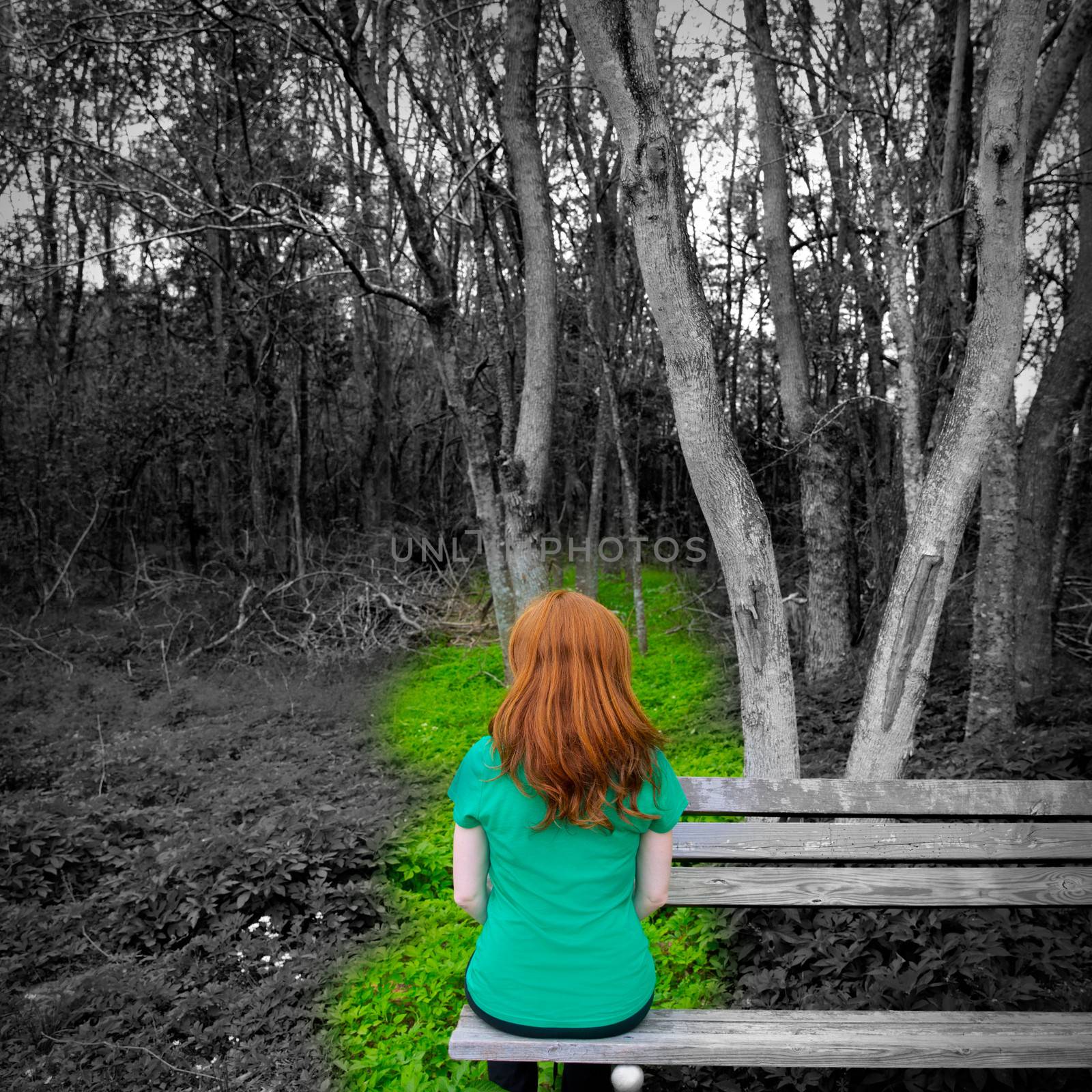 Lonely redhead woman rear view looking to forest sitting on a park bench