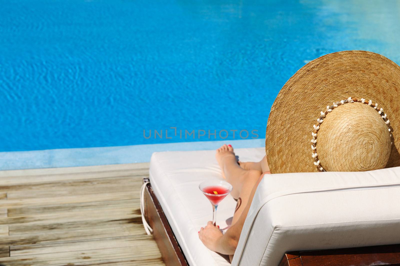 Woman in hat relaxing at the poolside with cosmopolitan cocktail