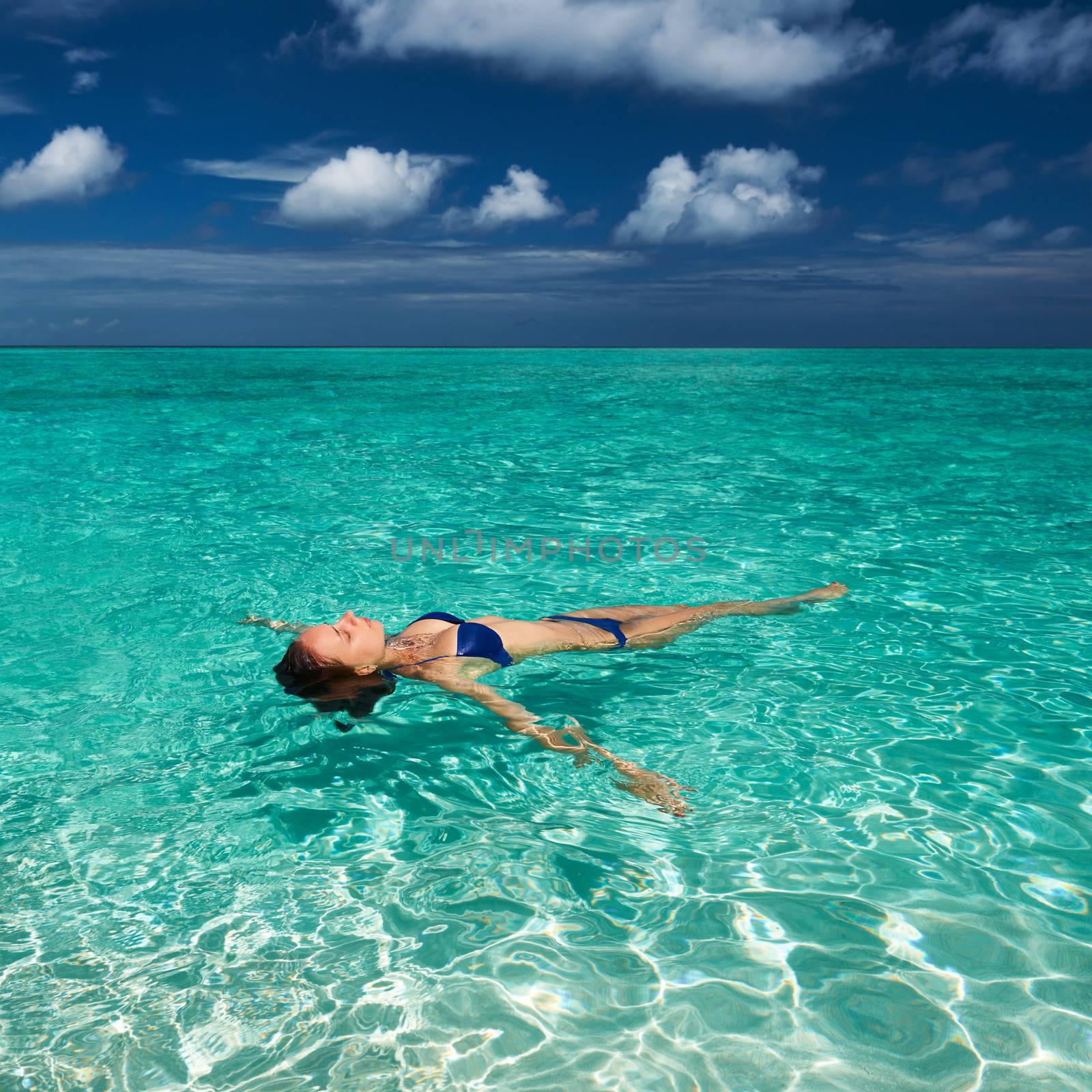 Woman in bikini lying on water at tropical beach