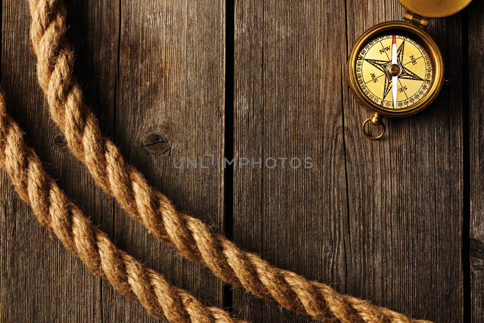 Antique brass compass and rope over wooden background