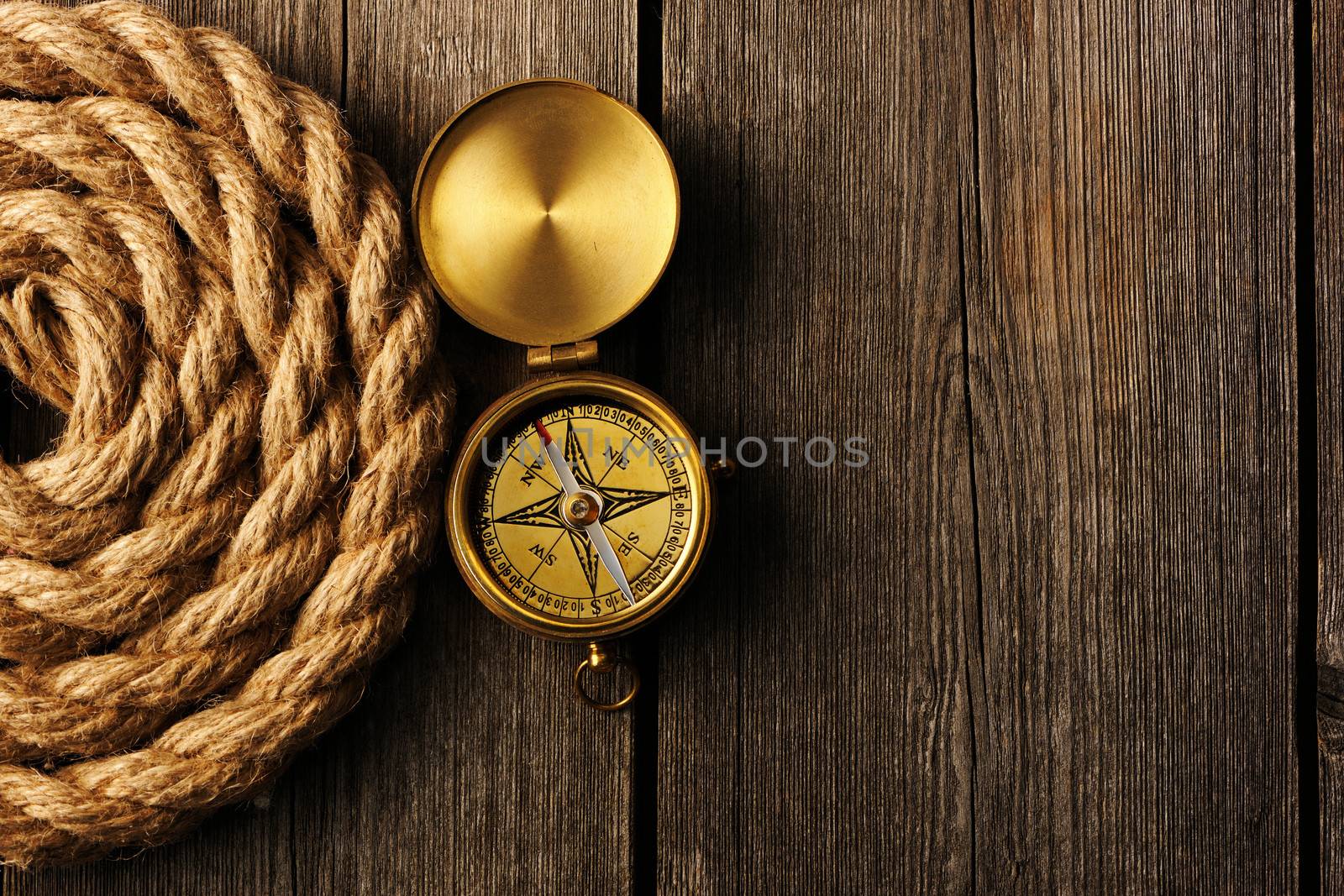 Antique brass compass and rope over wooden background