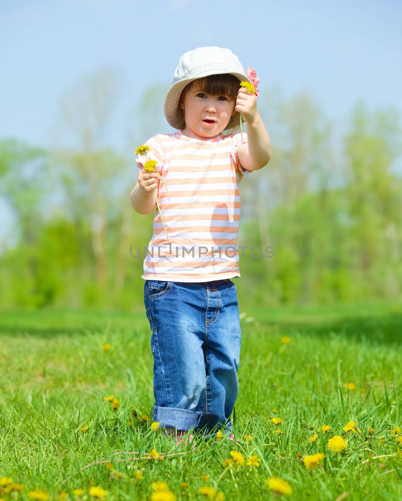 Sweet beautiful girl sitting on a green meadow with dandelions