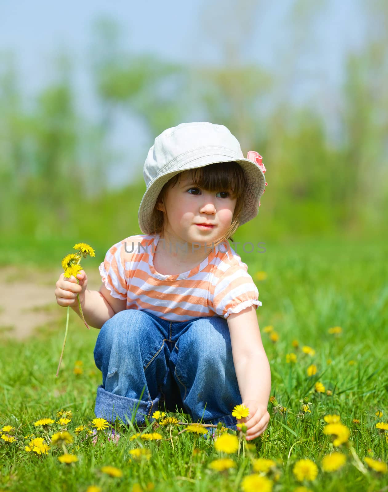 Sweet beautiful girl sitting on a green meadow with dandelions