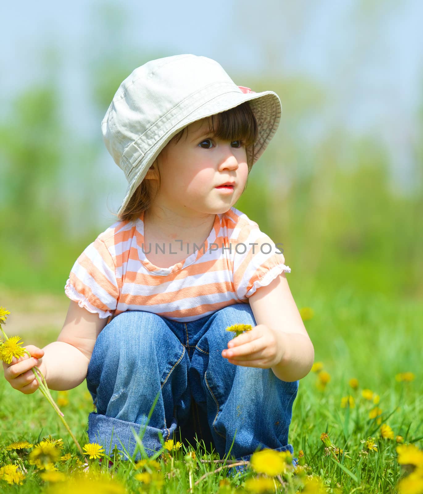 Sweet beautiful girl sitting on a green meadow with dandelions