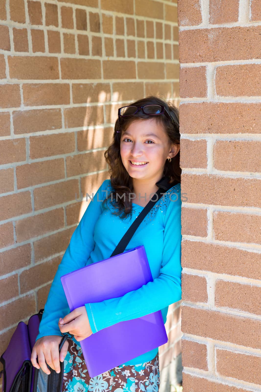 Schoolgirl teenager at school brick wall happy with folder and bag