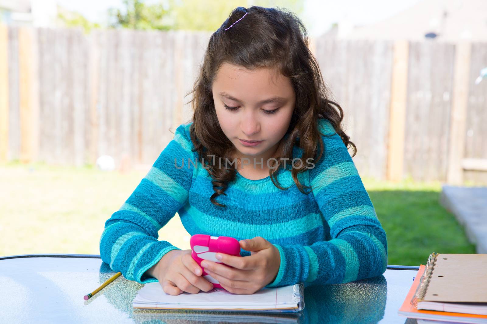 American latin teen girl with smartphone doing homework on backyard