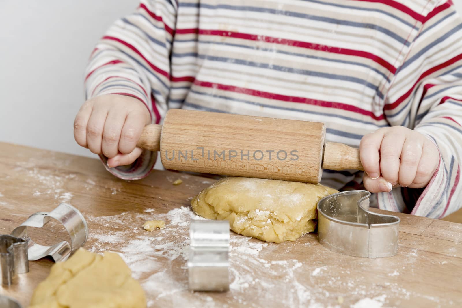 image of hands and desk. child is making cookies with a rolling pin