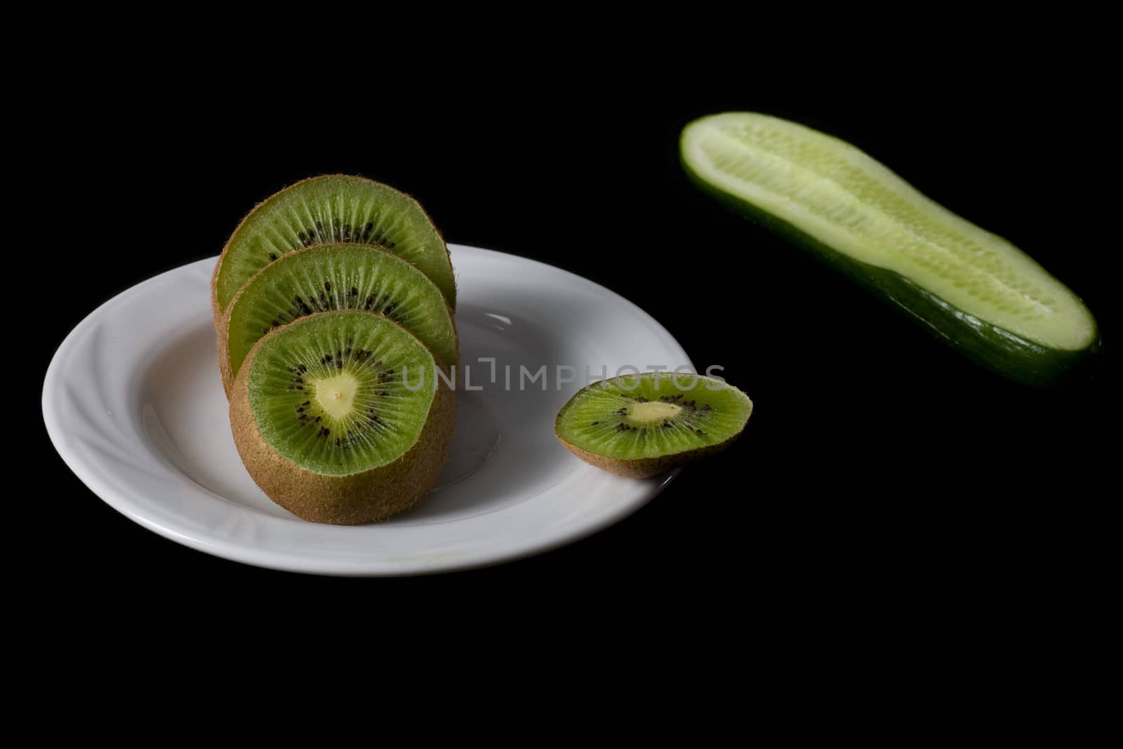 kiwi on white plate and cucumber isolated on black backgrownd  by foryouinf