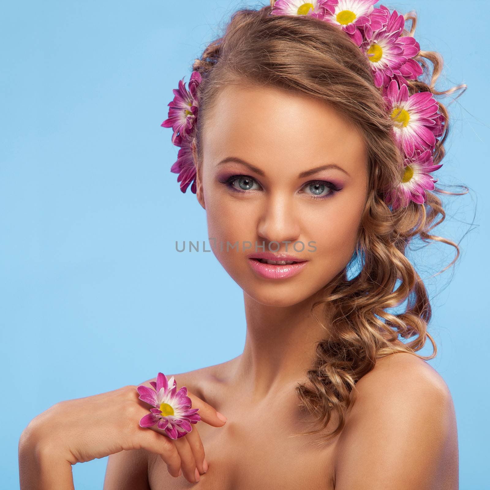 Beautiful young caucasian woman with flowers in her hair over blue background