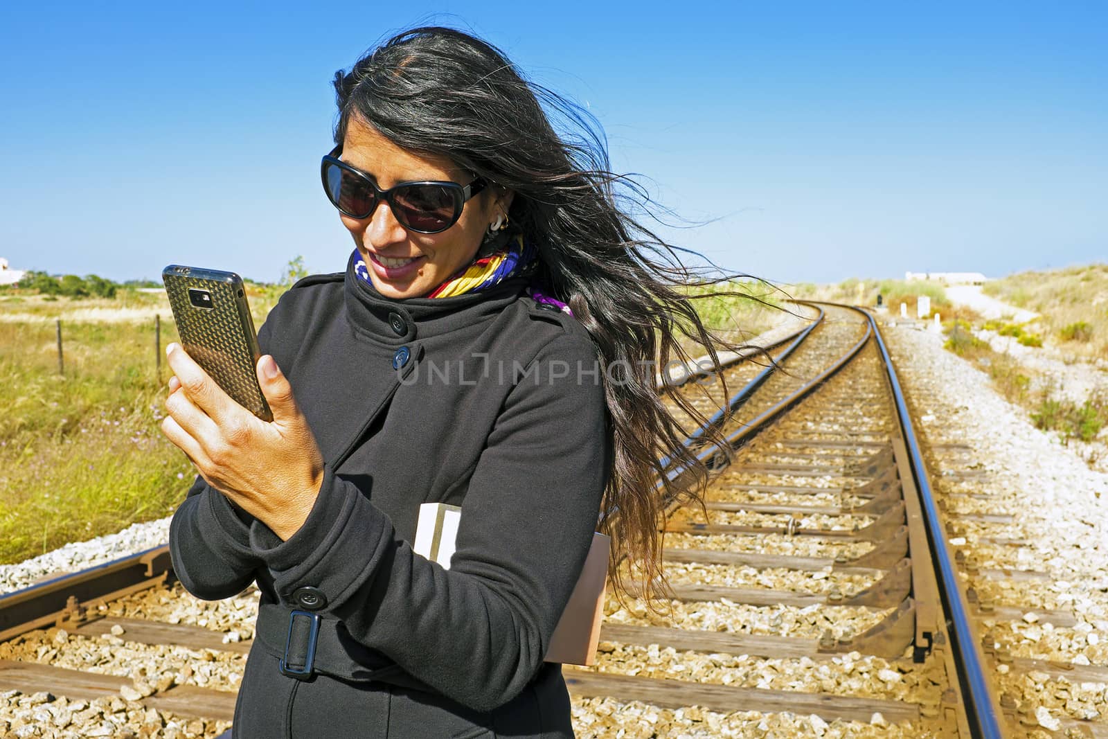 Young beautiful woman is writing a text message at a railroad track