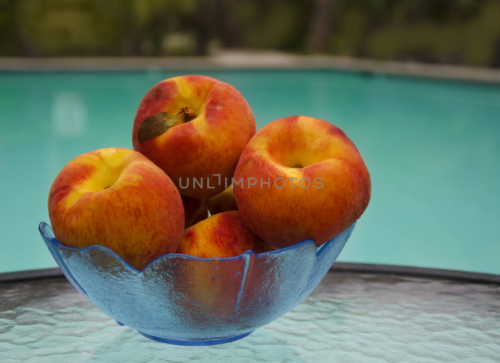 Peaches in a glass plate on table by the swimming pool
