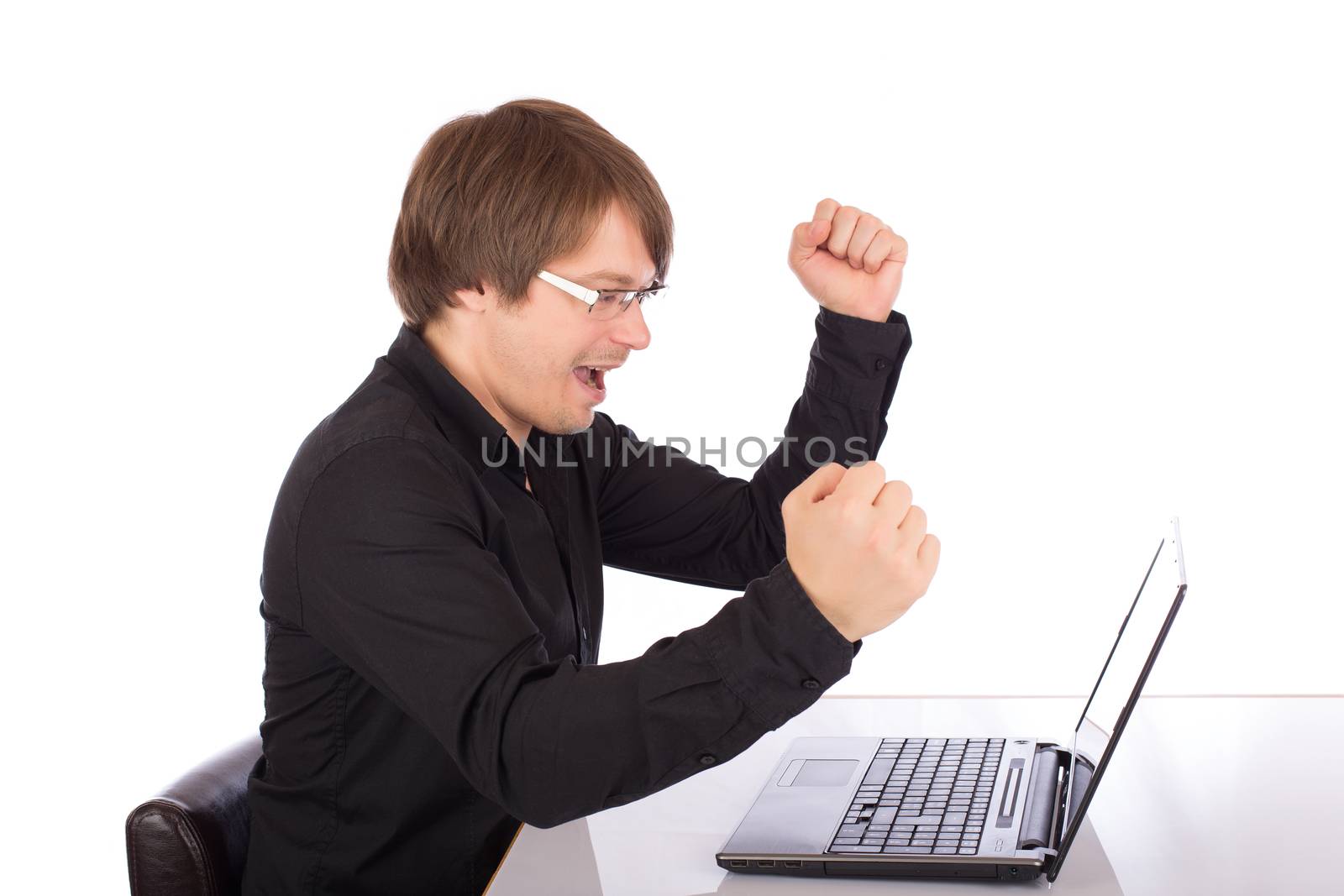 Happy business man cries victory and raises arms in front of his laptop. Isolated on white background.