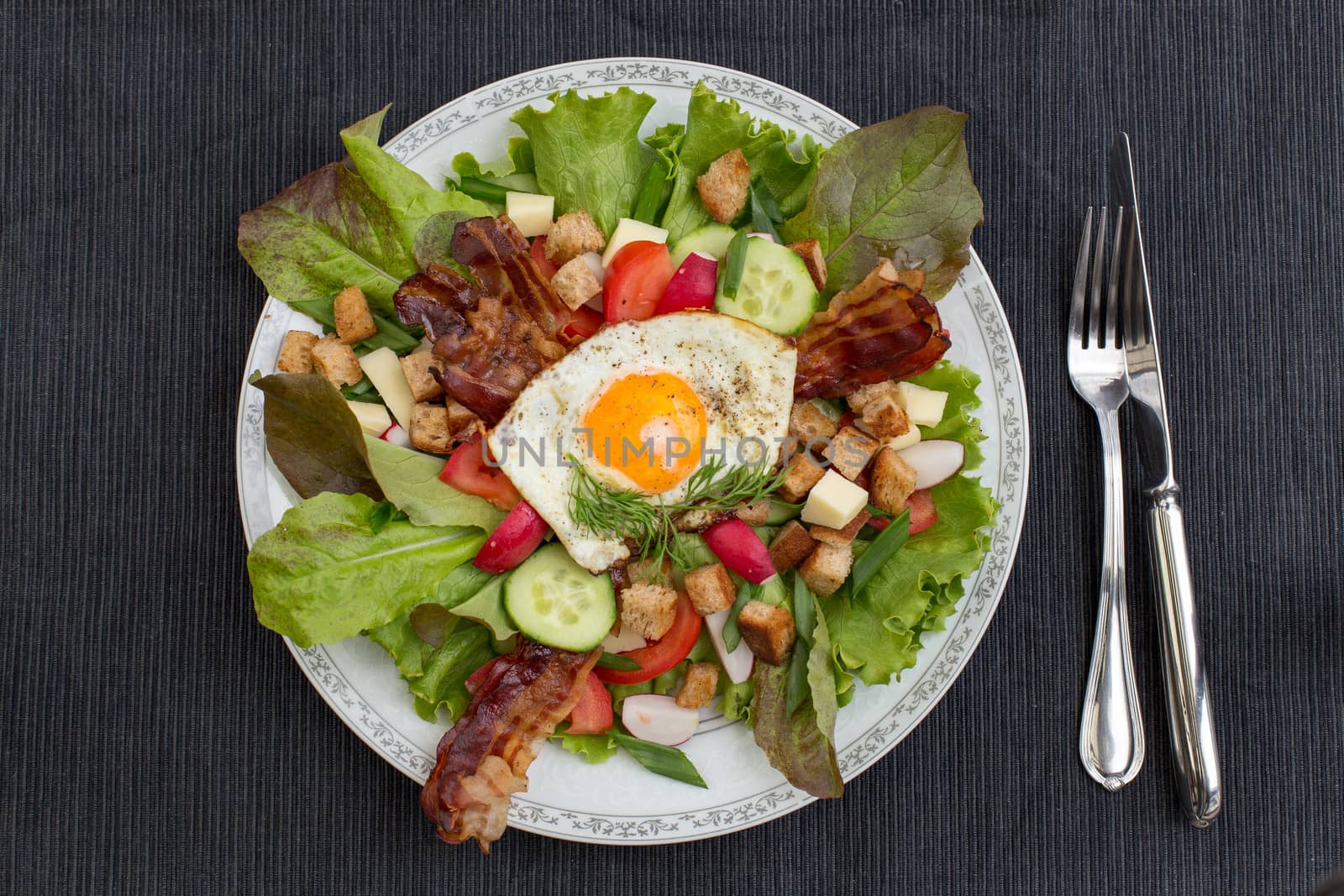 Fresh country salad also called peasant salad, greek salad or village salad. Composed with lettuce, cucumber, onion, radish, fried egg and bacon, cheese, tomatoes, parsley and croutons.