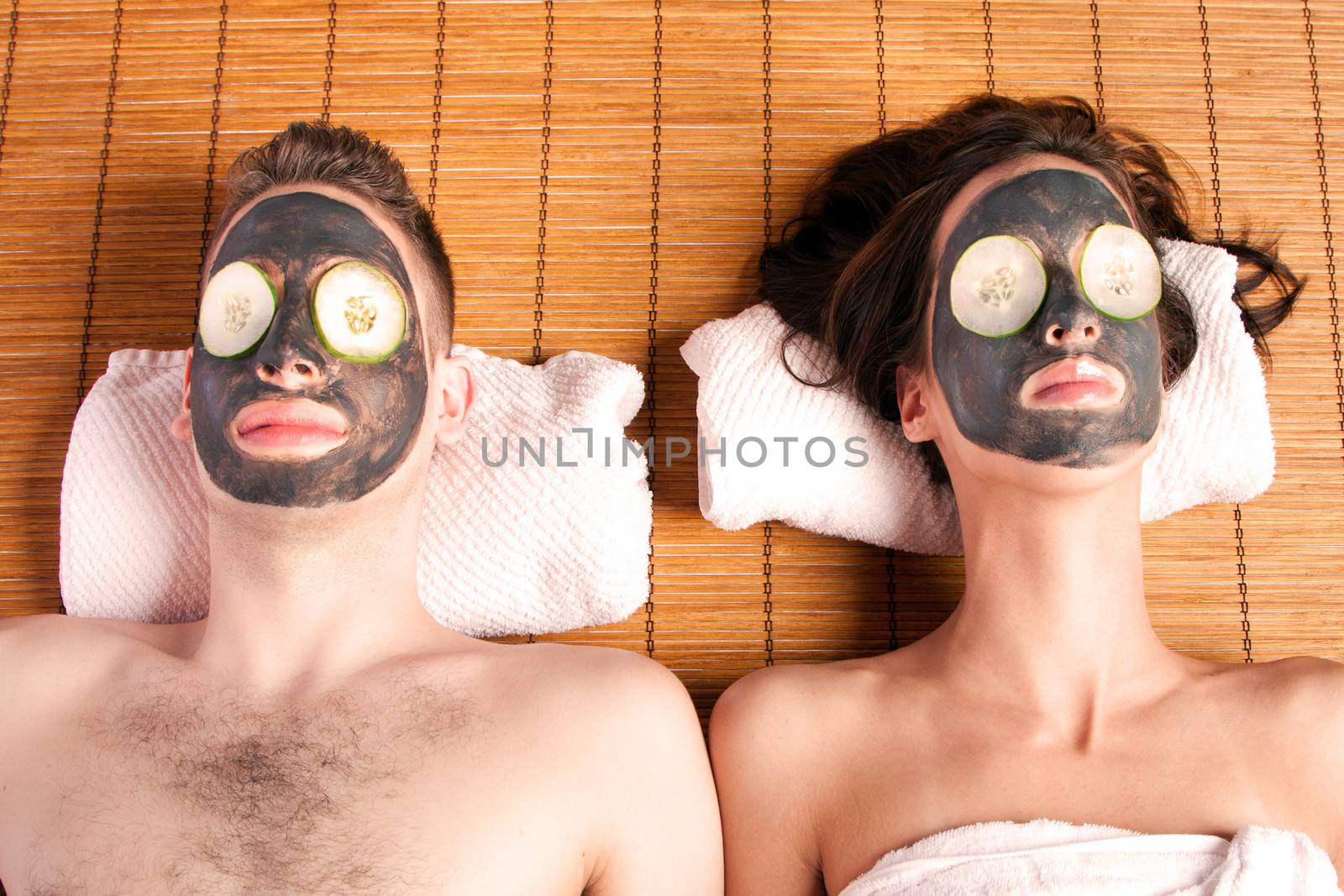 Couples holiday retreat at spa getting facial mask with cucumber skincare relaxing beauty treatment on bamboo.