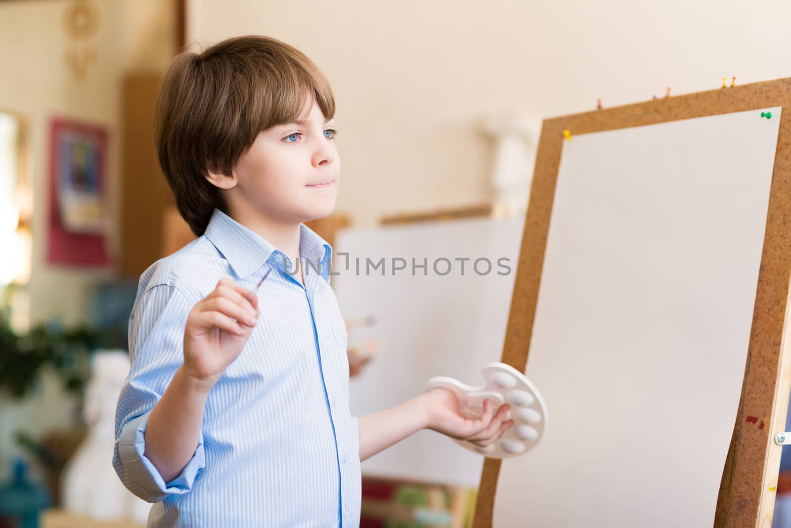 boy thinks, stands next to his easel, a drawing lesson