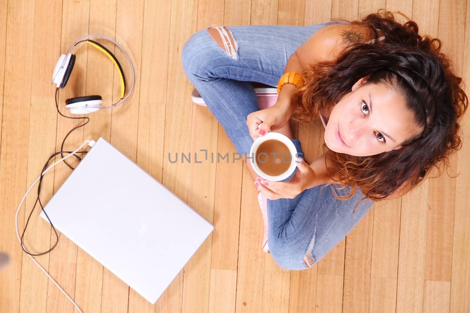 A girl sitting on the floor with a Laptop and some coffee.