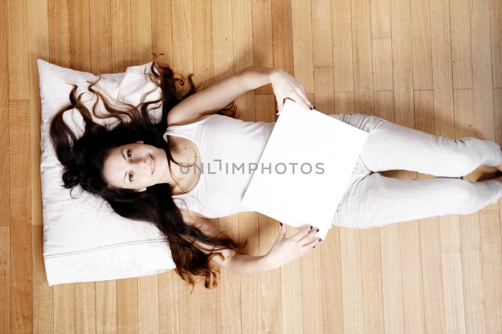 A young adult woman lying on the floor with a blank canvas.