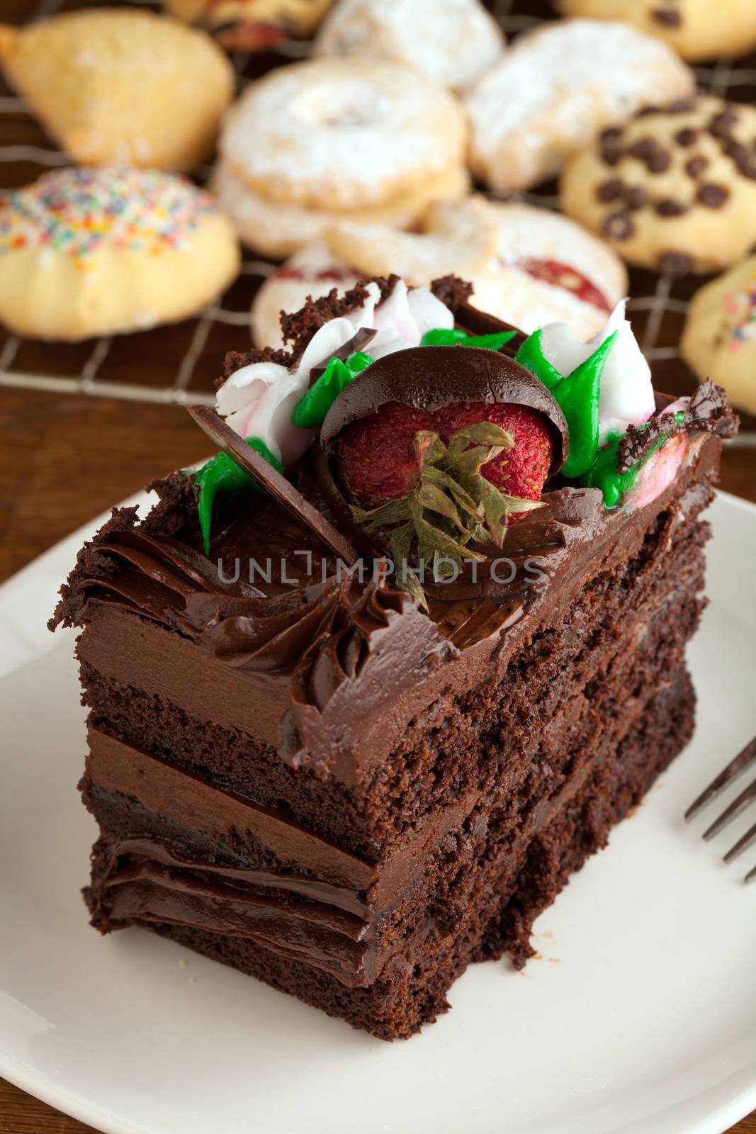 Italian cookies and a decadent slice of chocolate cake with iced flowers and chocolate covered strawberries on a plate with a fork.